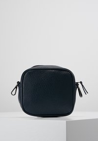 Kosmetická taška z kůže v tmavě modré barvě, čtvercového tvaru s texturovaným povrchem, vybavená zipovým uzávěrem a dvěma jezdečky na bocích.