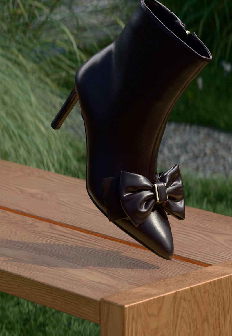 Bottine noire en cuir à talon haut avec un grand nœud décoratif, posée en équilibre sur un banc en bois à l'extérieur avec de la verdure en arrière-plan.