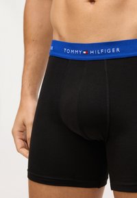 Czarne bawełniane bokserki z niebieskim elastycznym pasem z napisem i logo "TOMMY HILFIGER". Gładka tekstura, dopasowany krój.