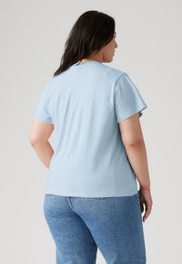 T-shirt en coton bleu clair à manches courtes, col rond et coupe décontractée, associé à un jean en denim. Pas de motifs ni d'accents visibles.