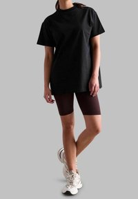 Sort bomulds-t-shirt med korte ærmer, parret med mørkebrune ribbede cykelshorts og klodsede hvide sneakers. Diskret logo på t-shirten.