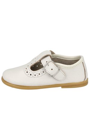 Zapato infantil tipo Mary Jane de cuero blanco con detalles perforados, correa ajustable con hebilla plateada y suela de goma marrón claro.