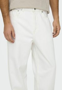 Pantalones vaqueros de mezclilla blanca con un ajuste relajado, presentan costuras amarillas y herrajes plateados. Los bolsillos en la parte delantera y trasera añaden funcionalidad.