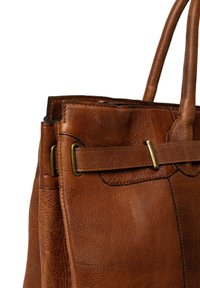 Borsa in pelle marrone con manici robusti, accenti in ottone e cuciture visibili, mostrata da vicino su uno sfondo bianco.
