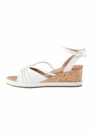 White wedge sandals with a cork heel, featuring a knotted front design, buckle ankle strap, and smooth leather texture.