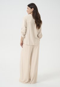 Beige, løst siddende top med lange ærmer og en buet kant, parret med matchende brede bukser. Letvægtsstof med glat tekstur.