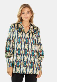 Blusa multicolor con un patrón geométrico en tonos verde azulado, rojo y beige. Hecha de una tela suave con un corte relajado y cierre de botones.