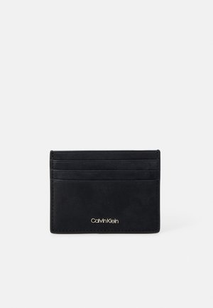 Porte-cartes en cuir noir avec quatre emplacements, finition texturée et logo de la marque en relief en bas, présentant un design épuré et un matériel minimal.