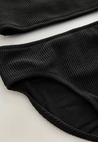 Completo bikini nero in tessuto a coste testurizzate. Il top ha una fascia larga; il fondo presenta un interno liscio e bordi elasticizzati.