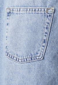 Bolsillo de denim azul claro con un contorno cosido, que presenta una textura suave y patrones desvaídos, ubicado en el lado derecho de la tela.
