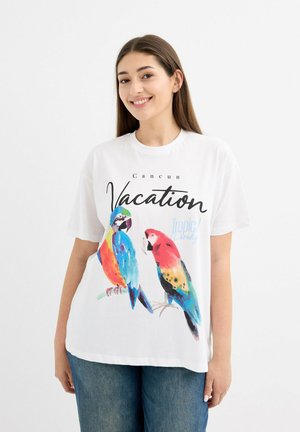 Camiseta blanca de algodón con un gráfico colorido de dos loros y el texto "Vacaciones en Cancún" y "Paraíso Tropical" en negro.