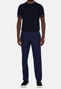 Mörkblå kortärmad t-shirt med vit kant, tillsammans med rymliga mörkblå byxor. Modellen står i svarta sneakers.