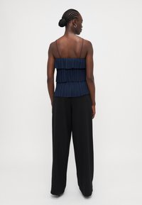 Navy pleated top with two layered ruffles, adjustable thin straps, paired with wide black trousers. Smooth texture and simple design.