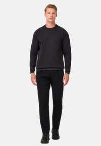 Črna majica s kapuco z raglan rokavi, okroglim izrezom in rebrastimi manšetami, v kombinaciji s črnimi hlačami in črnimi športnimi copati. Preprost, minimalističen dizajn.