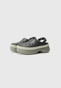 Black clogs with a textured surface, multiple ventilation holes, and an adjustable heel strap, featuring a contrasting beige sole.