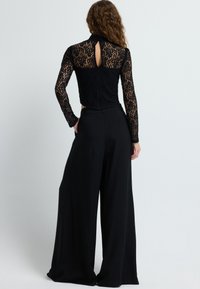 Mustapitsilla varustettu paita pitkähihaisilla hihoilla ja avonaisella selkäosalla, yhdistettynä leveään mustaan housupariin. Paita sisältää monimutkaista pitsiyksityiskohtaa.