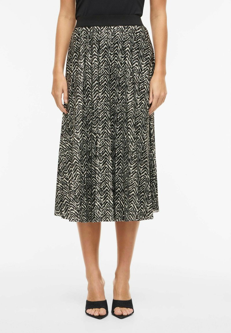 Midi spódnica w czarno-kremowy wzór z motywem jodełki, elastyczną talią i zwiewnym materiałem, zestawiona z czarnymi sandałkami na otwartym palcu.