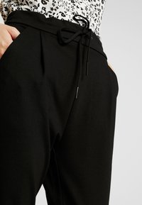 Černé kalhoty z měkké látky, s elastickým pasem na tkaničku a bočními kapsami, navržené s sklady pro uvolněný střih.