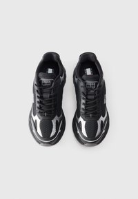 Black athletic sneakers with mesh upper, contrasting silver accents, thick black sole, and lace-up design. Features logo on tongue and side.