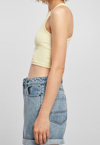 Żółty prążkowany crop top z szerokimi wycięciami na ramionach, w połączeniu z jasnoniebieskimi szortami z wysokim stanem z denimu, które mają podwinięte nogawki i kontrastowe szwy.