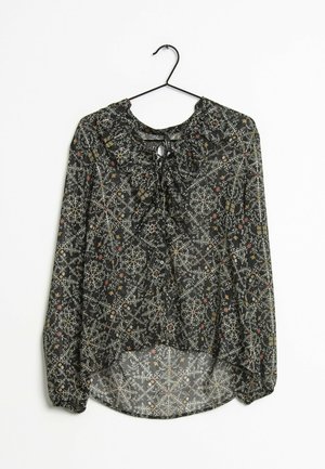 Blusa nera trasparente con vari motivi floreali e geometrici, caratterizzata da un colletto rotondo, dettagli con fiocco e maniche lunghe elasticizzate.