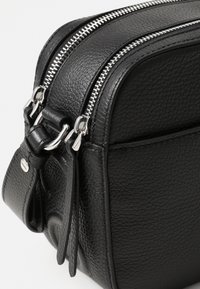Borsa in pelle nera con superficie testurizzata, doppi zip argentati e accessori lucidi. Presenta una forma strutturata e un design snello.