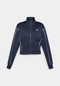 Marinblå kort zip-jacka i slätt tyg, med hög krage, silverdetaljer längs ärmarna och en liten logotyp på bröstet.