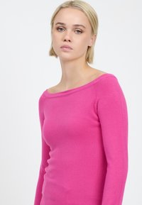 Maglione aderente a maniche lunghe in un vivace colore rosa, con scollatura a spalle scoperte e texture liscia. Senza motivi visibili né accessori.