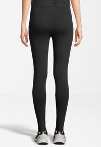 Leggings negros hechos de una tela elástica, diseño ajustado, con una textura suave y cortes en los tobillos. Combinados con zapatillas deportivas grises.
