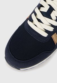 Navy blue athletic shoe featuring a textured mesh upper and beige accents, with cream laces and a cushioned sole.
