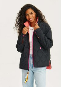 Přesně quiltovaný černý kabát s růžovými akcenty, zapínání na zip a boční kapsy. Má korálovou podšívku a dekorativní třásně na zipu.