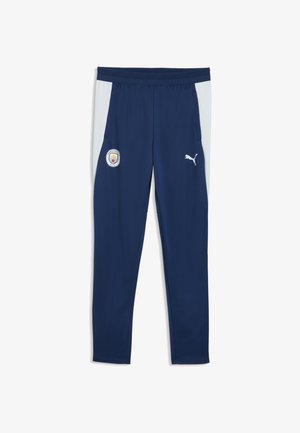 Granatowe spodnie sportowe z jasnoszarymi panelami bocznymi, logo Manchester City na lewym udzie oraz biały logo Puma na prawym udzie.