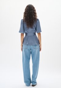 Blå blus med korta utställda ärmar och knytband i midjan, tillsammans med löst sittande ljusblå jeans med bakfickor och avslappnad passform.