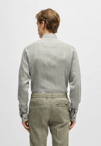 Camicia grigia chiaro a maniche lunghe con una sottile texture e polsini abbottonati, abbinata a pantaloni verdi oliva texturizzati con tasche posteriori.