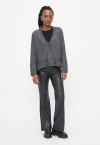 Grå strikket cardigan med V-hals, frontknapper, to lommer og dekorative nagler langs kragen og lommene. Kombinert med sorte lærbukser.