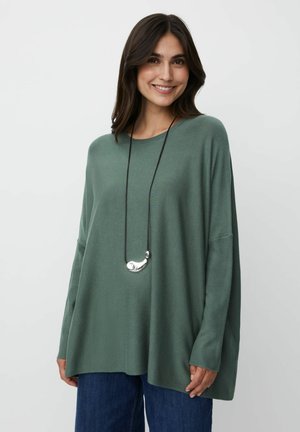 Overdimensioneret grøn strikket sweater med lange ærmer, der har en design med sideslids, parret med en sort snor og en sølv vedhængs kæde.
