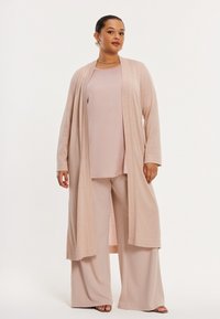 Langer, hellrosa Cardigan über einem passenden Oberteil und weiten Hosen. Der Cardigan hat eine offene Vorderseite und einen weichen, strukturierten Stoff.