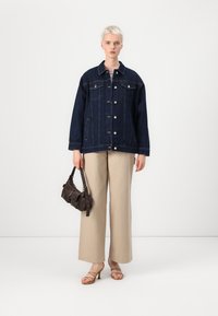 Temno modra denim jakna z oversized krojem in srebrnimi gumbi, bež široke hlače in majhna črna torbica. Gladke teksture in sproščen kroj.