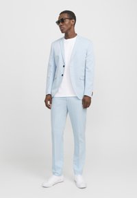 Svetlo moder kostim s slim fit dizajnom, sako s jednim dugmetom in dvema gumboma. Združeno z belim majico in belimi športnimi čevlji.