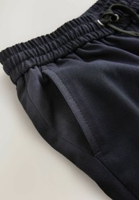 Shorts de sport noirs avec une taille élastique, un cordon de serrage et des poches latérales. Tissu lisse avec une finition propre et des détails de couture minimaux.