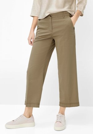 Personne portant un pantalon large kaki court avec des poches et des baskets rose clair sur fond blanc.