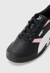 Sorte Puma-sneakers med hvite og rosa detaljer, sydd dekor, svarte lisser og teksturert såle synlig mot en lys bakgrunn.