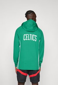 Grøn hættetrøje med "CELTICS" i hvid skrift på ryggen. Har hvide sidelæg og er lavet af tekstureret stof.