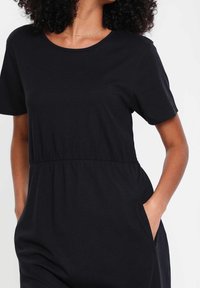 Robe courte à manches courtes noire en coton doux, dotée d'une taille cintrée et de poches latérales, avec un col rond et une coupe décontractée.