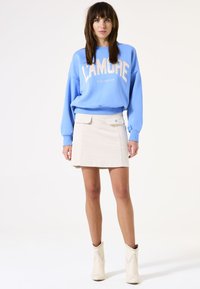 Sudadera azul claro con estampado "LAMORE", combinada con una falda corta color crema que cuenta con bolsillos. Botines blancos con acentos de tachuelas.