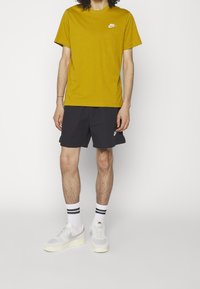 Žluté tričko Nike, jednofarebné; černé šortky; bílé ponožky s černými pruhy; šedé tenisky Nike; neformální oblečení.