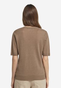 Kortærmet brun sweater, strikket tekstur, rund halsåbning, ribbede manchetter og kant, afslappet pasform, iført med lyse bukser.