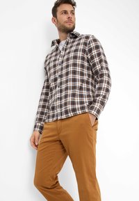 Karierte Hemd mit Knopfleiste in dunklem Braun, Weiß und Blau, mit langen Ärmeln und lockerem Schnitt, kombiniert mit braunen Hosen.