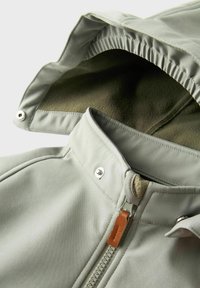 Lichtgrijze jacket met een fleece-voering in de kraag, zichtbare rits met leren trekband, en knopsluitingen. Glad textuur, praktische ontwerp.