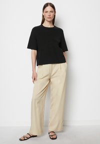 Schwarzer Kurzarm-Pulli, lockere Passform, kombiniert mit beigen, weiten Hosen und schwarzen flachen Sandalen. Schlichtes modernes Design, ohne sichtbare Muster.